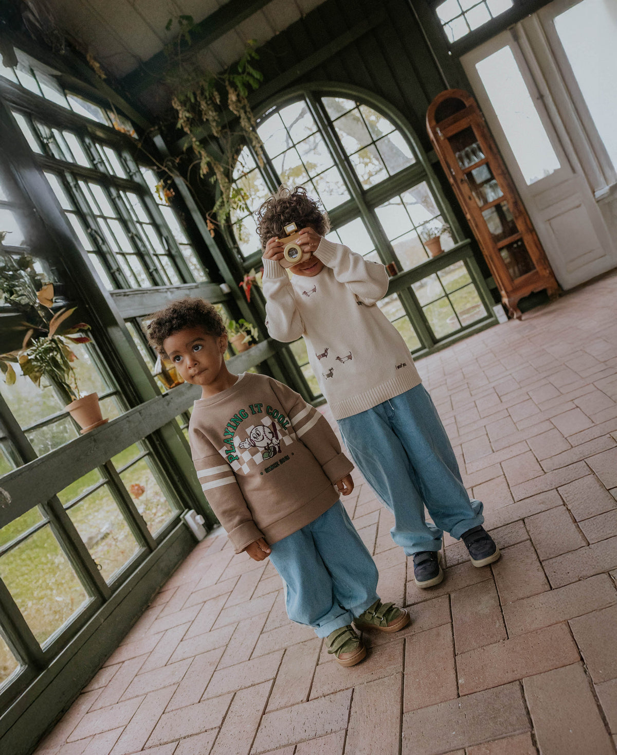 Two children in a tiled conservatory, one in the Alvin Cool Sweatshirt