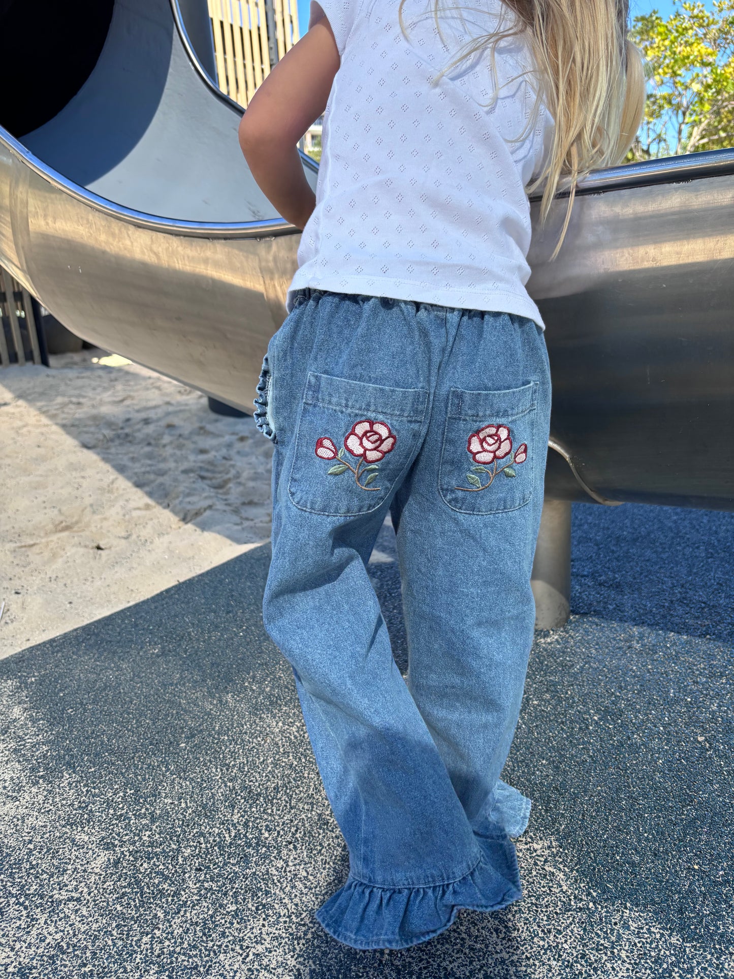 Child at a playground slide in the Don Rose Pant, rose back pockets and ruffle hem showing