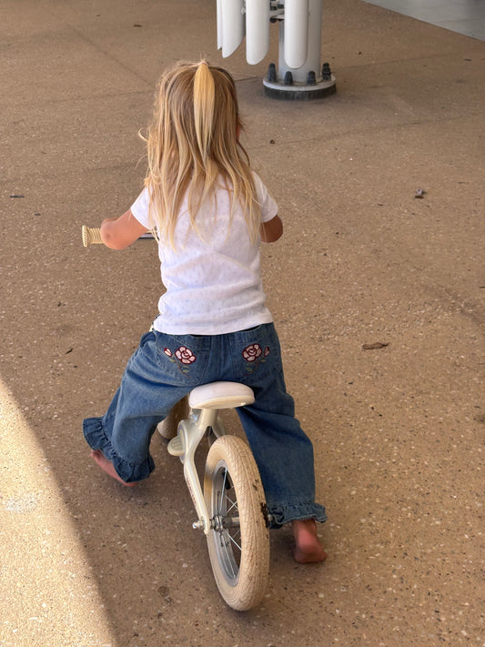 Child on a balance bike in the Don Rose Pant, embroidered roses on the back pockets