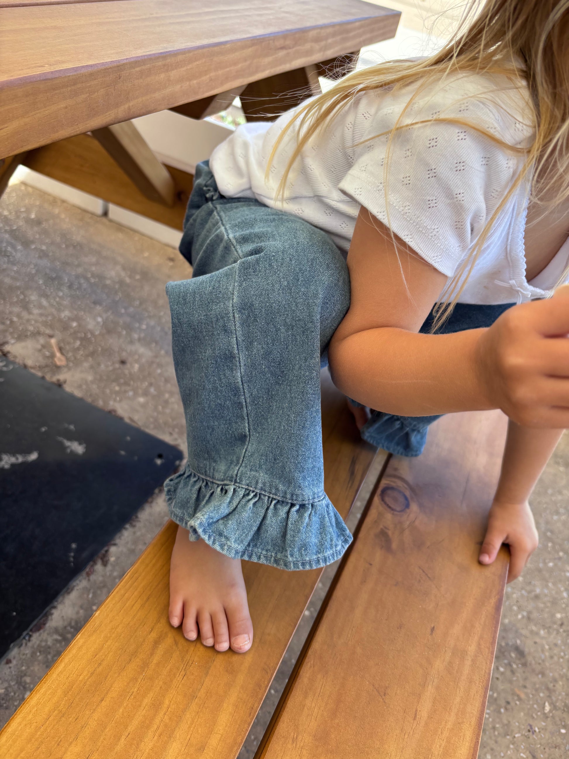 Close-up of the Don Rose Pant ruffle hem, child barefoot on a bench