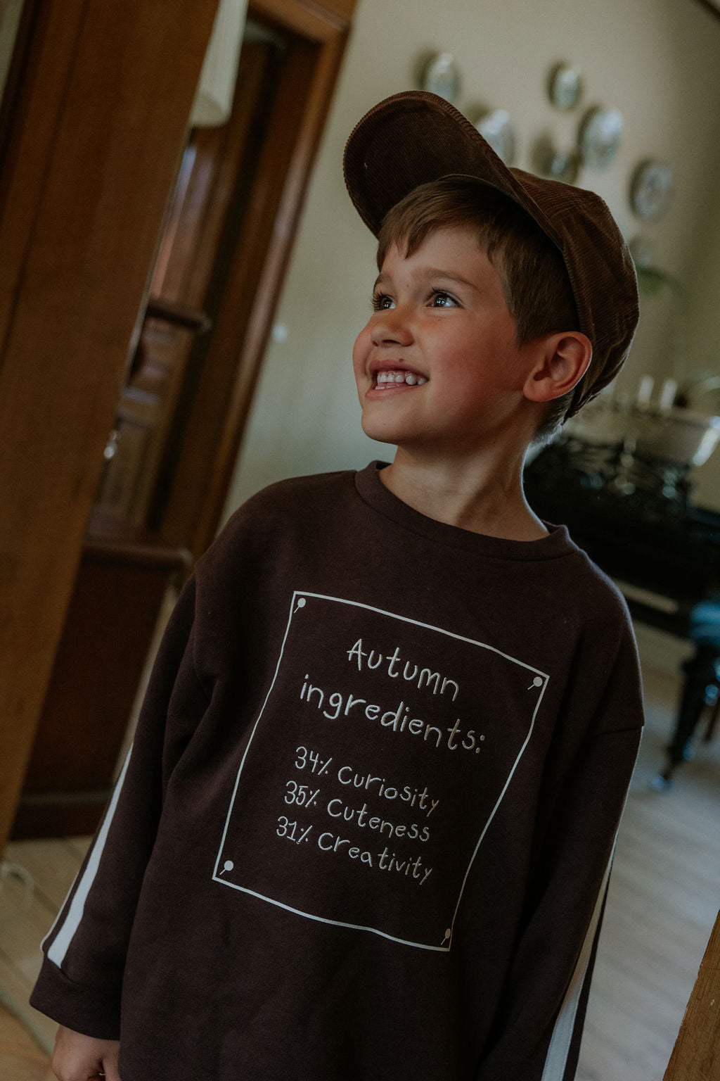 Smiling child in the brown Kamma Cap and a dark 'Autumn ingredients' sweatshirt