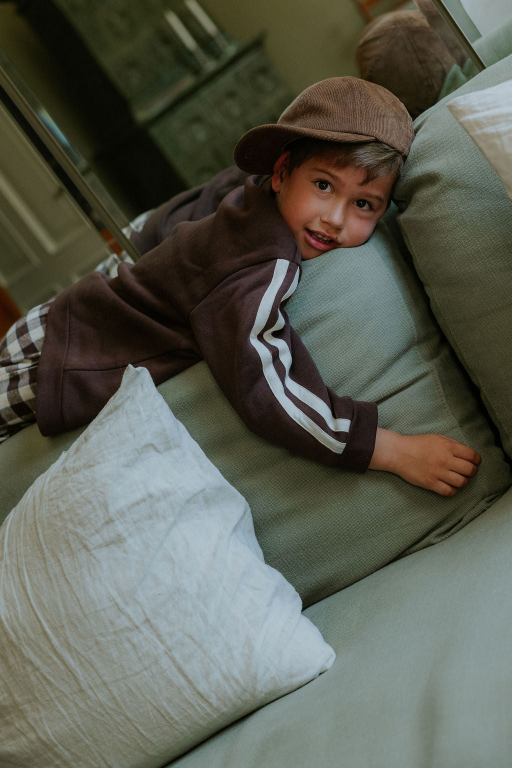 Child lying on a sofa in the brown Kamma Cap and a striped track top