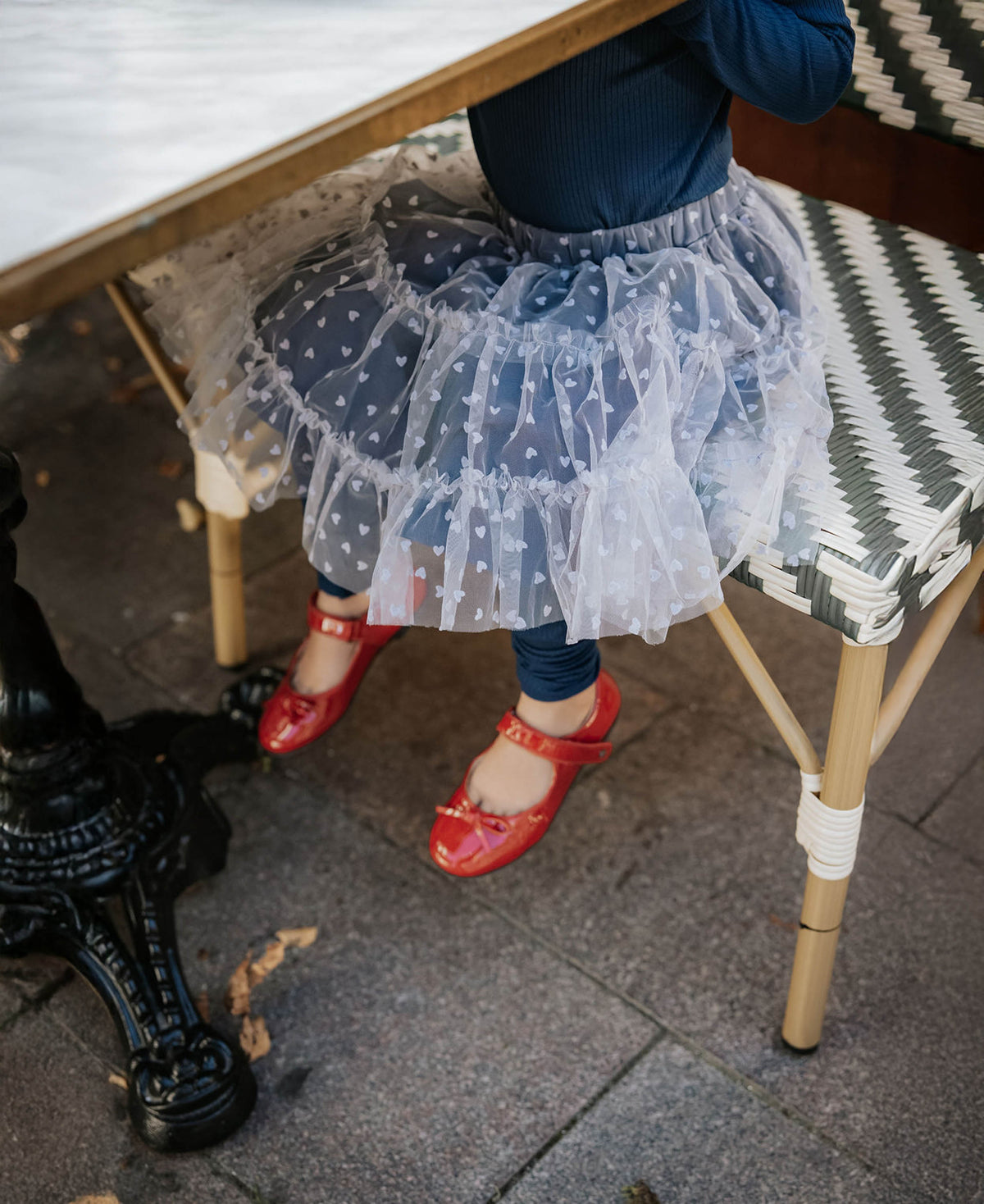 Close-up of the heart-print tulle layers and red shoes under a café chair