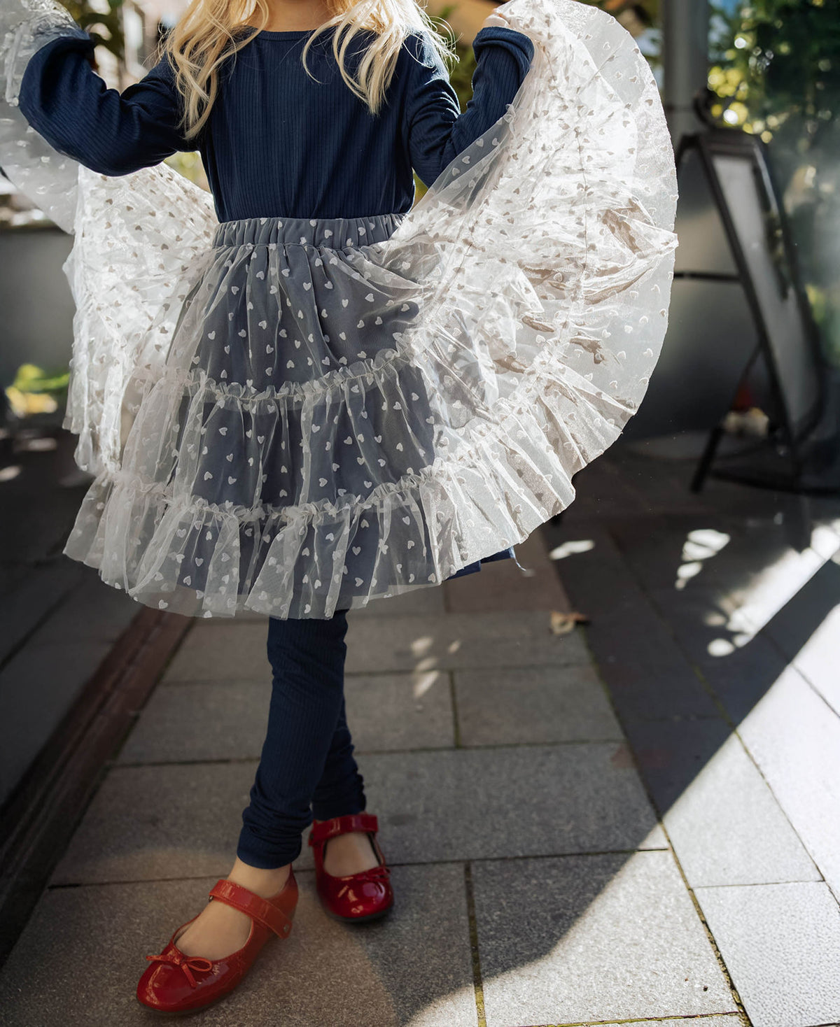Child twirling in the Slate Tulle Skirt with navy tights and red shoes, seen from behind