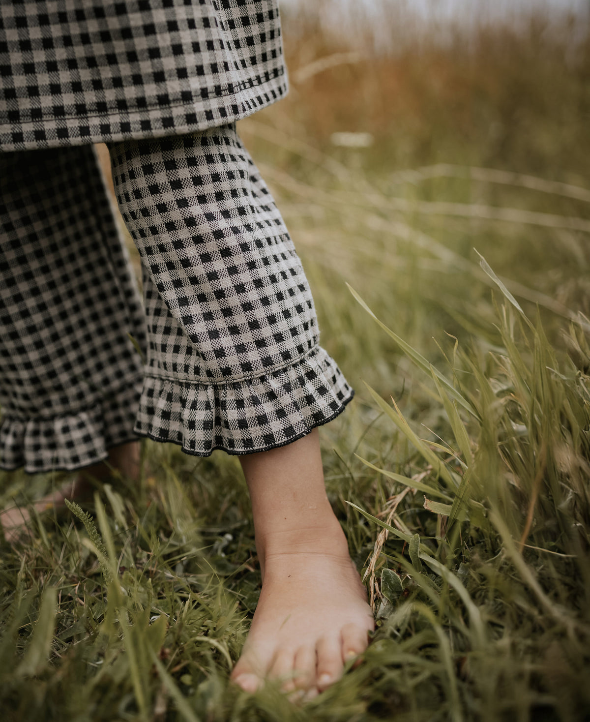 Close-up of a gingham ruffle hem and a bare foot in long grass