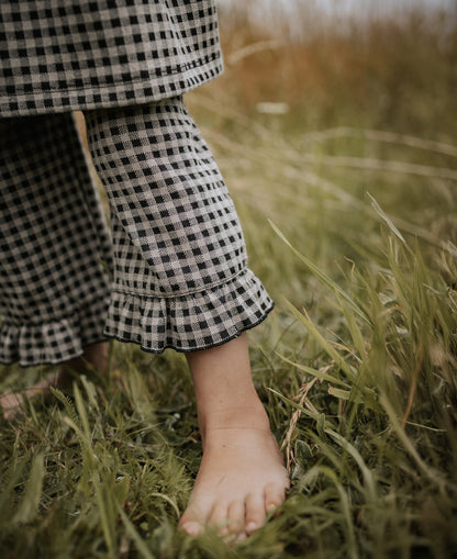 Close-up of a gingham ruffle hem and a bare foot in long grass