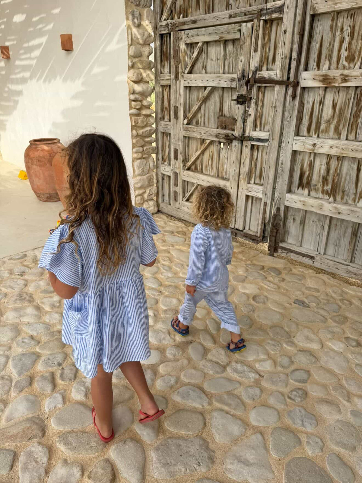 Two children walking across a cobbled courtyard, one in the blue striped Cha Cha Dress