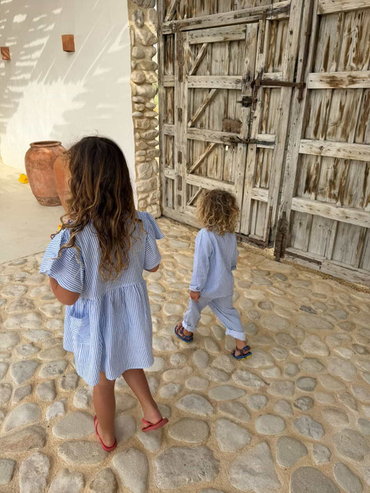Two children walking across a cobbled courtyard, one in the blue striped Cha Cha Dress