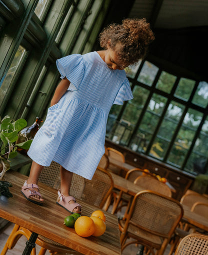 Child standing on a wooden table in the Cha Cha Dress, flutter sleeves and pockets showing