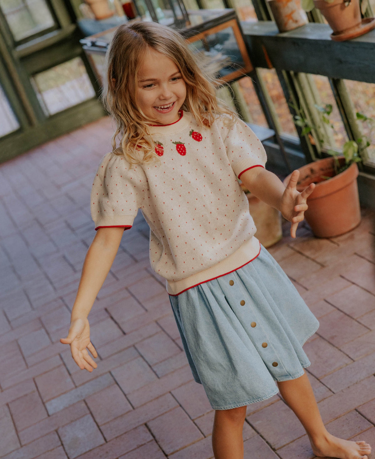 Child dancing in a conservatory in the Don Denim Skirt and a knitted top