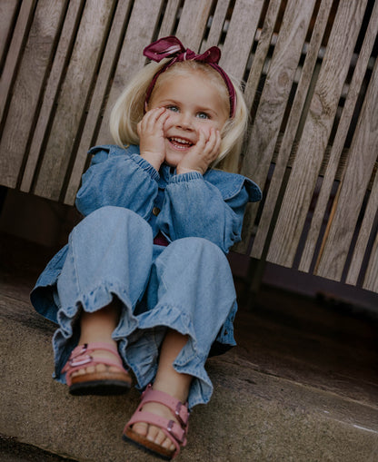 Smiling child sitting on a bench in the Don Rose Pant and a denim top