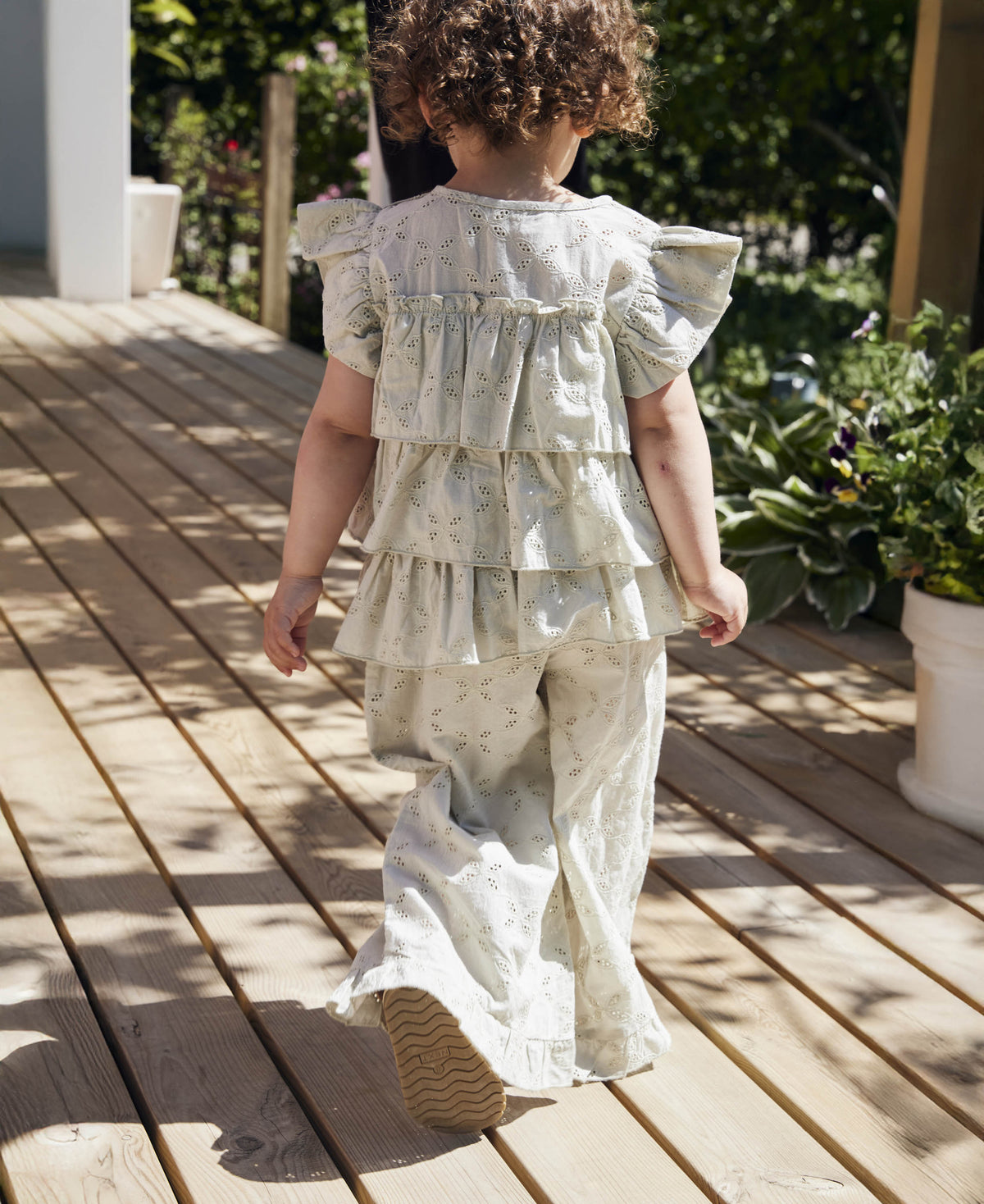Child walking along a timber deck in a sage ruffle top and the Harper Ruffle Pant, seen from behind