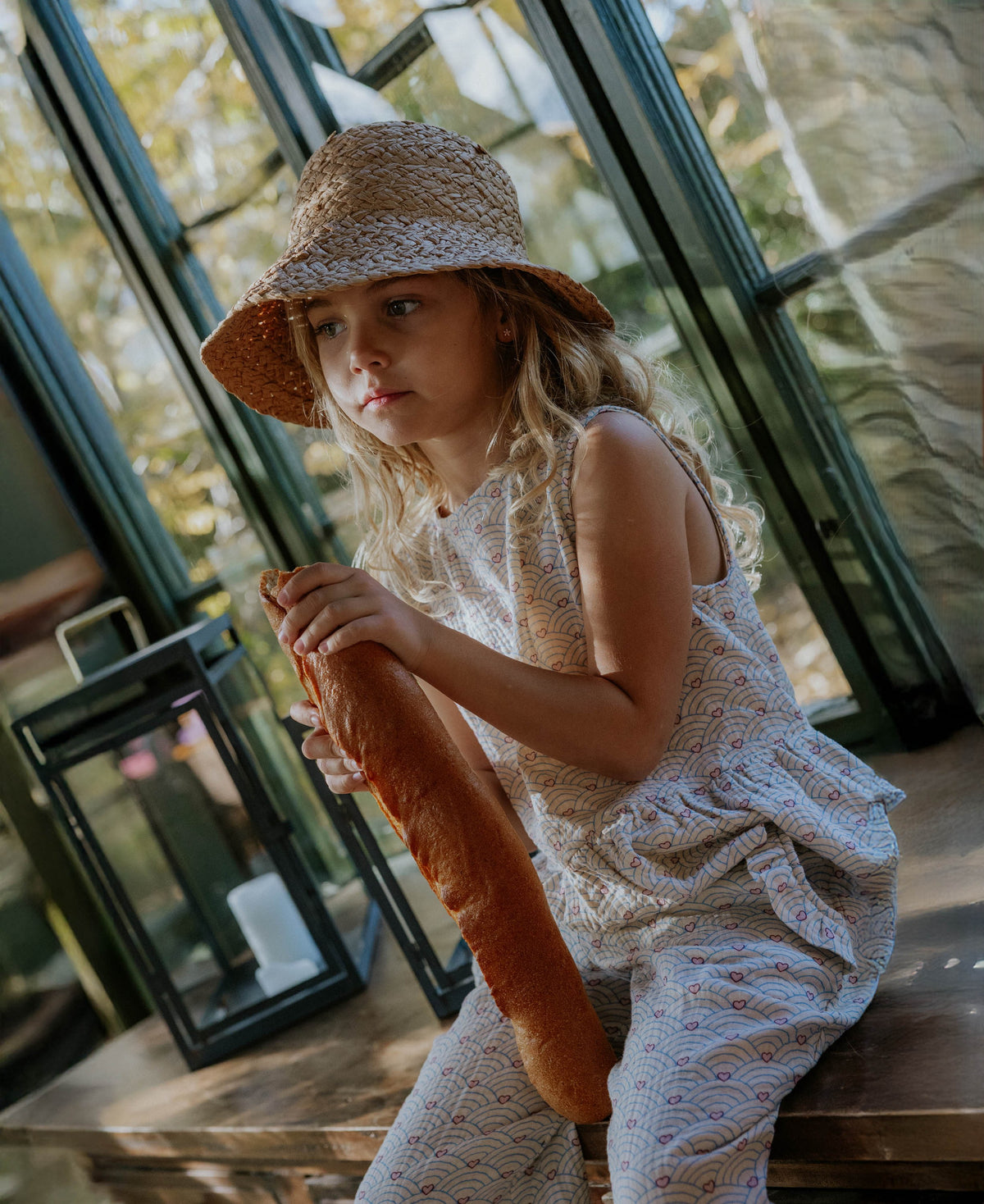 Child in a woven sun hat and the cream Bridget Top, sitting by a window