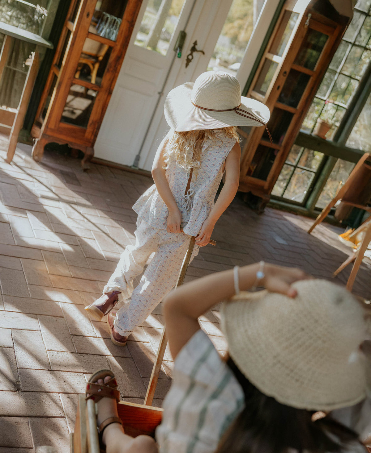 Child in a sun hat wearing the Bridget Top in a sunlit room