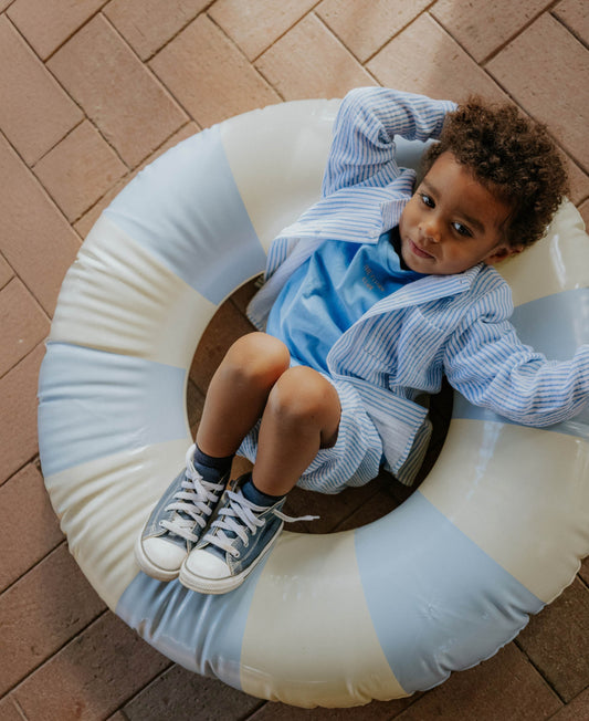 Child lounging in a striped pool ring in the blue Sommer Club T-shirt and striped shorts