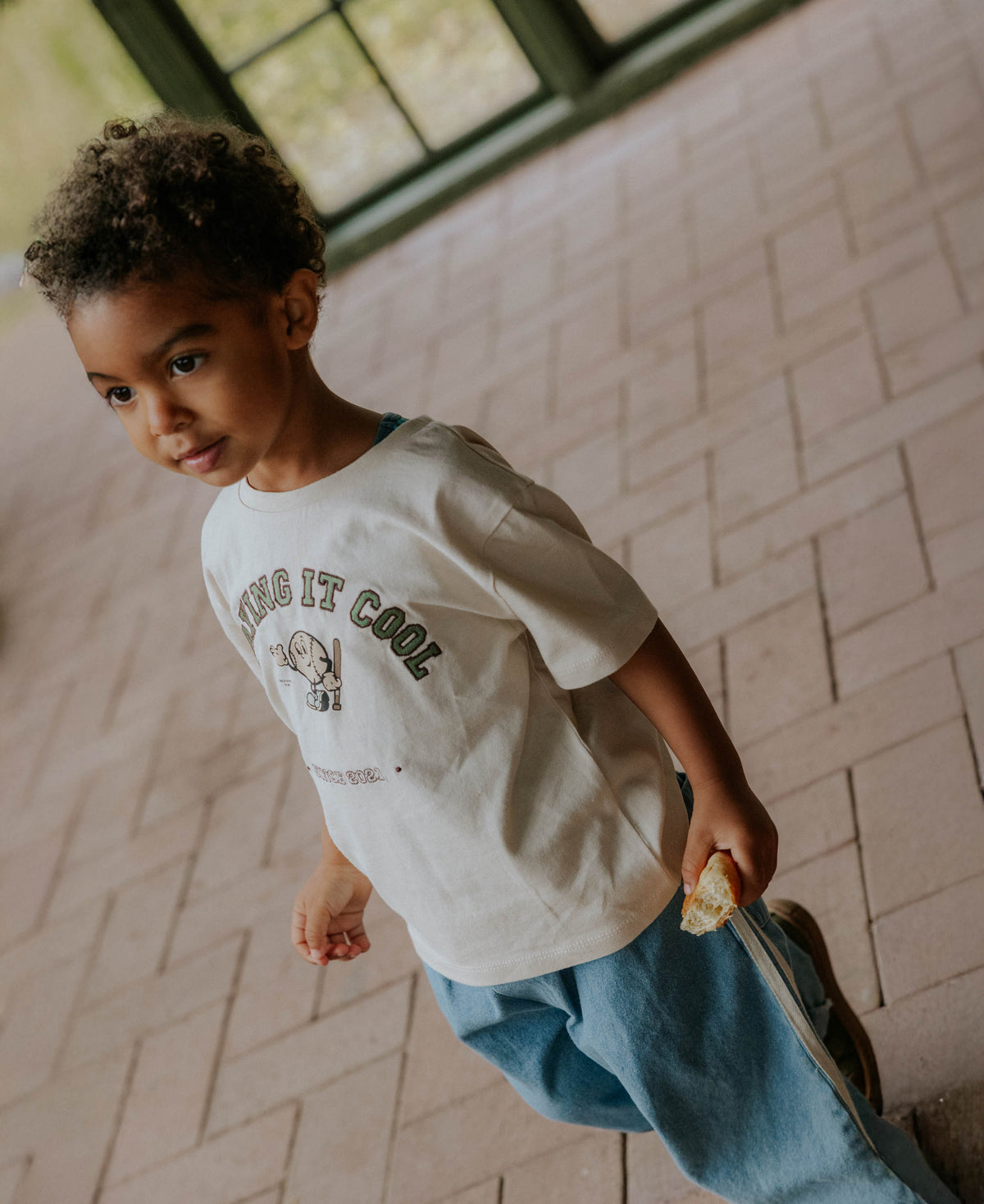 Child walking across a tiled floor in the Sommer Cool T-shirt and jeans
