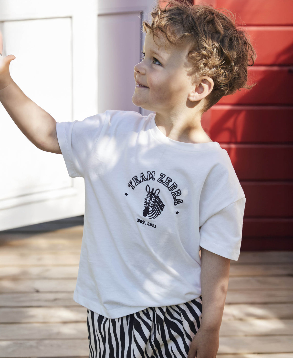 Child outdoors in the Team Zebra t-shirt and zebra print trousers, reaching upward