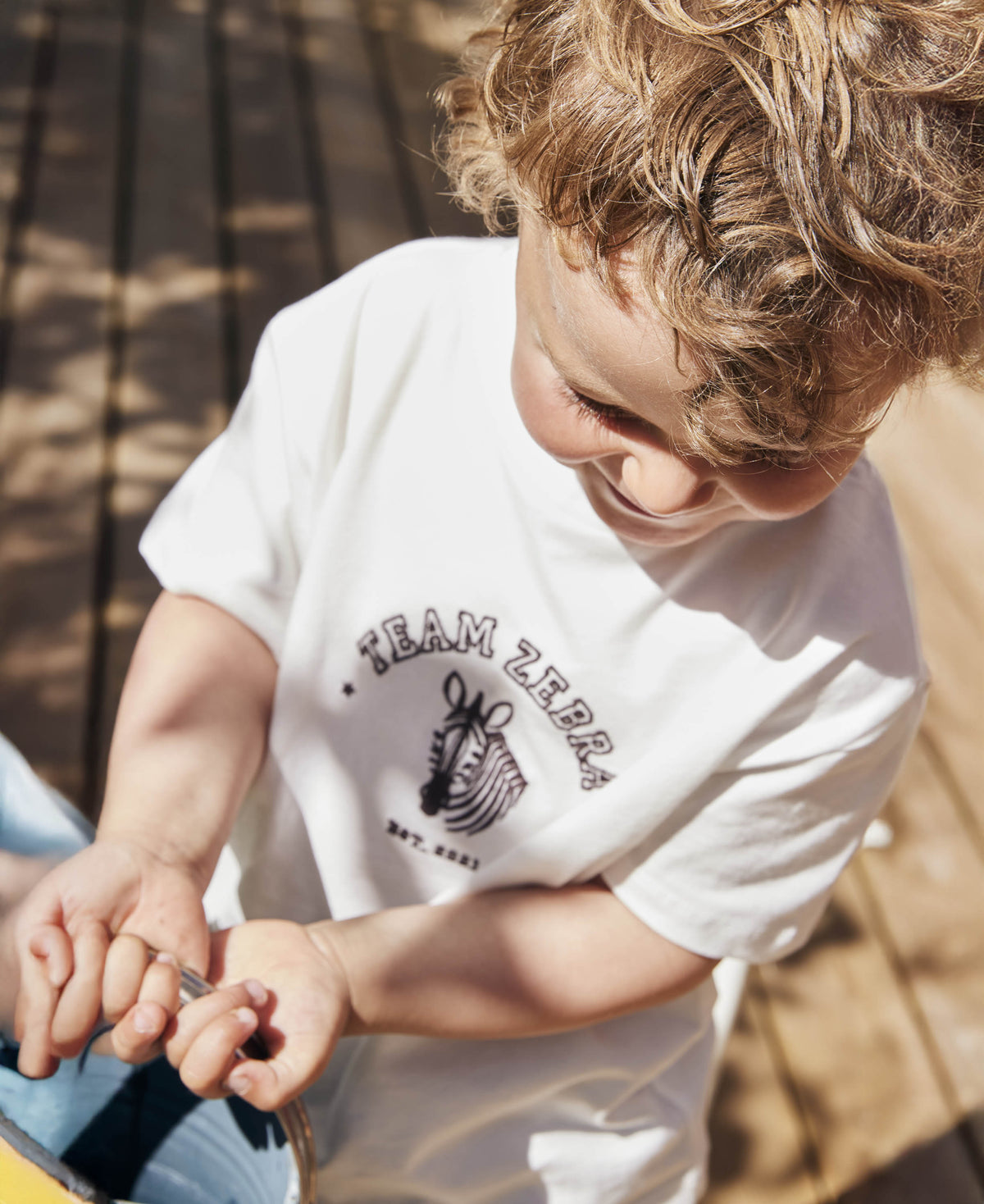 Child sitting outdoors in the Team Zebra t-shirt, looking down at their hands