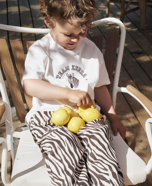 Child in the Team Zebra t-shirt and zebra print trousers, sitting in a chair with lemons