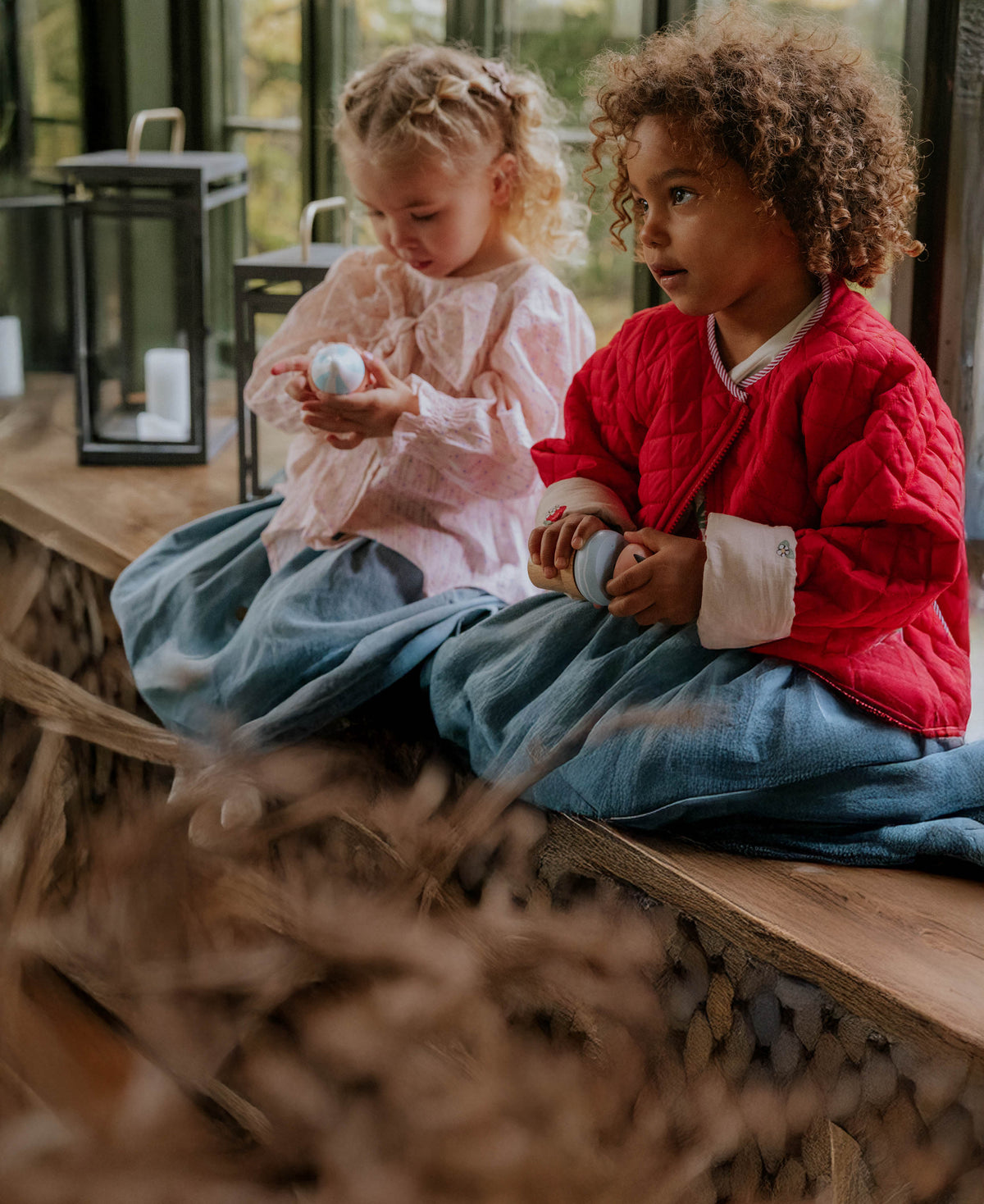 Two children sitting on a wooden step, one in the chalk pink bow blouse with denim trousers