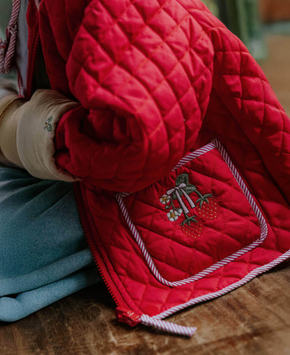 Close-up of the embroidered strawberry pocket and striped binding on the red quilted jacket