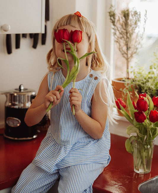 Girl in a blue and white striped Cha Cha top and matching trousers, sitting on a kitchen bench holding red tulips