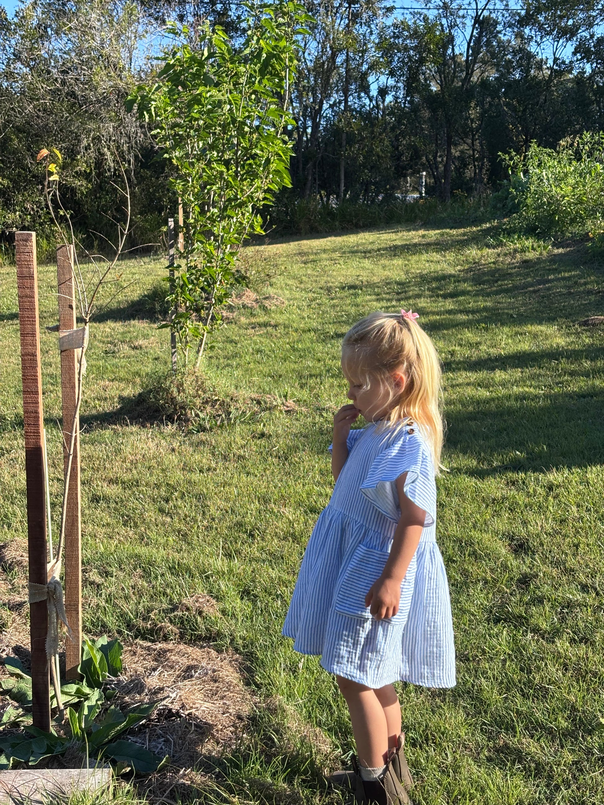 Child in a sunny garden wearing the blue striped Cha Cha Dress