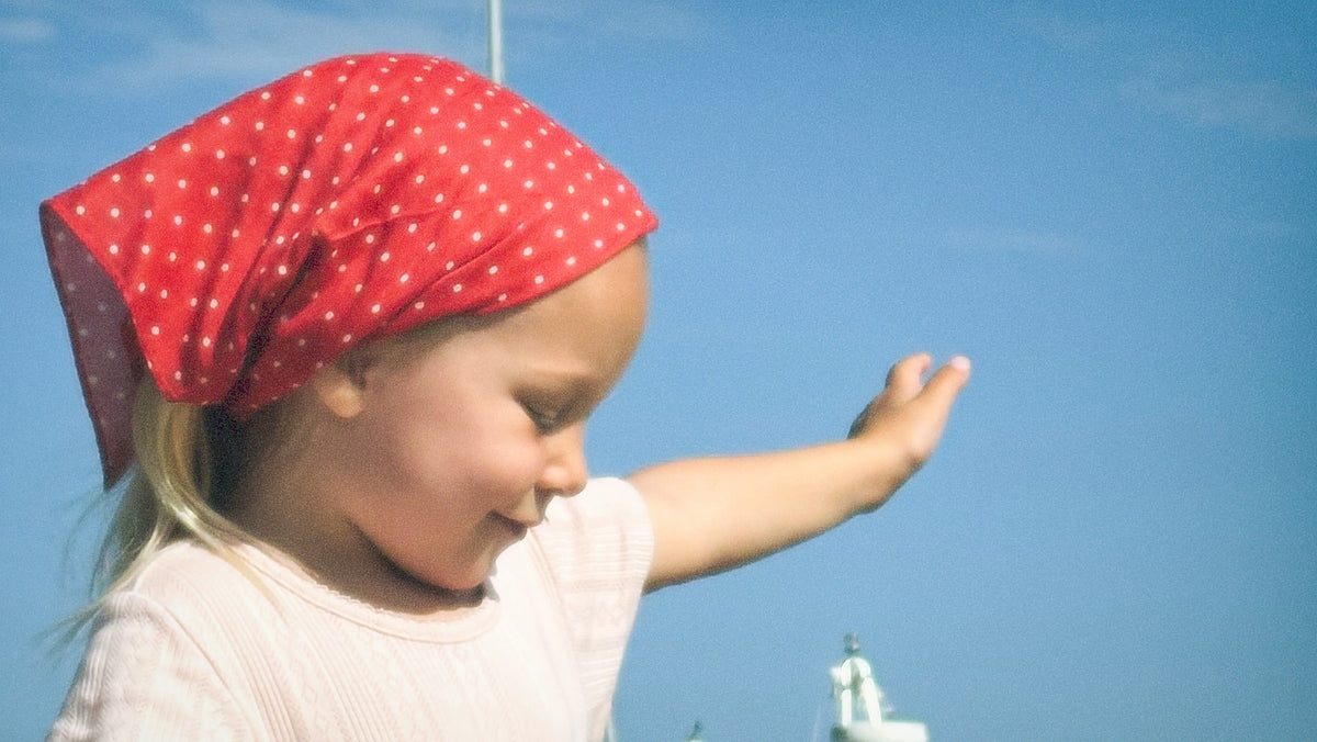 Girl wearing a red polka dot headscarf on the beach — Maeval kids clothing Australia.